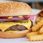Close-up of a juicy cheeseburger with sesame seed bun and crinkle-cut fries for fast food trivia.