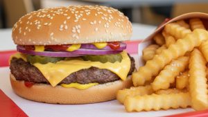 Close-up of a juicy cheeseburger with sesame seed bun and crinkle-cut fries for fast food trivia.
